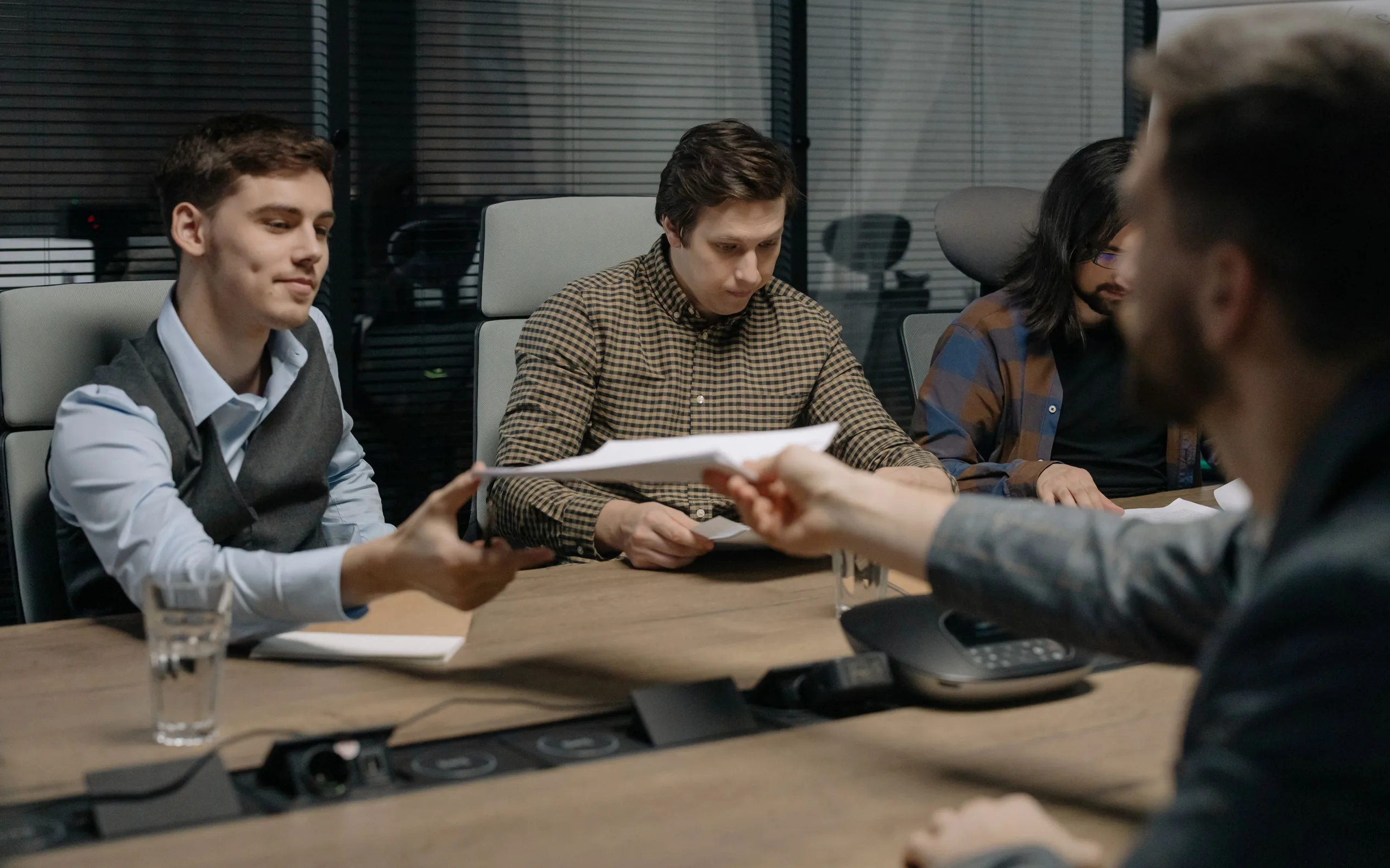 Quatre personnes autour d’une table échangent des documents pendant une réunion de direction.